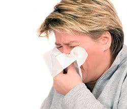 Man sneezing into a Kleenex from allergies or sensitivities. One our Edmonton Naturopaths is trained to help reduce or eliminate their effects.